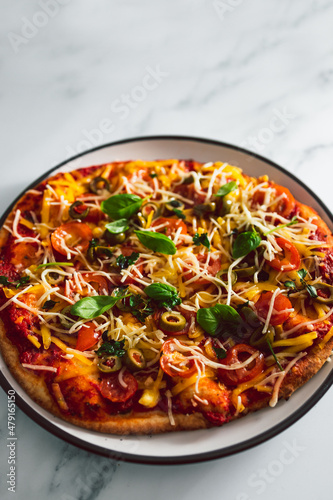 vegan homemade pizza with cherry tomatoes olives and fresh herbs topped with dairy-free cheese, healthy plant-based food