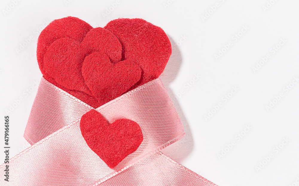 Fototapeta premium A lot of red felt hearts with a pink ribbon bow isolated on a white background on the left