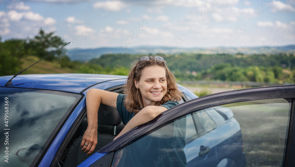 Portrait of a beautiful young woman on the background of car and summer landscape