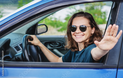 Beautiful young woman in sunglasses smiling and looking at the camera driving a car