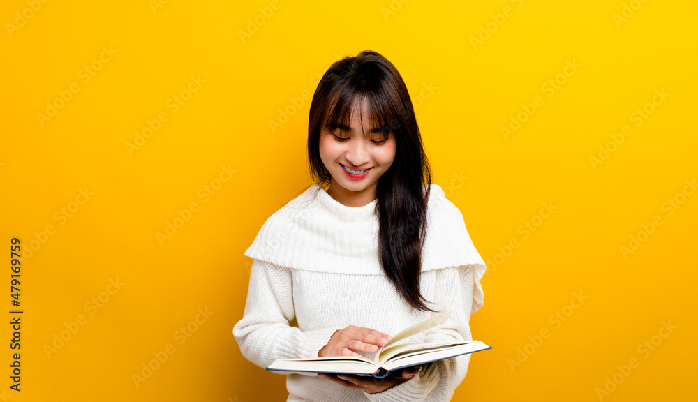 Fototapeta premium photo of asian girl smiling while reading a book while smiling on a yellow background book reading concept a little girl who loves to read books