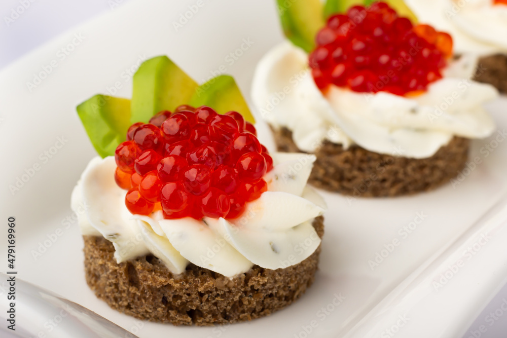 Close-up of luxurious canapés, crowned with glistening red caviar, paired with a velvety cream base, all presented on a rye canvas, highlighting culinary finesse. Smorrebrod. Canapes with red caviar Close-up of luxurious canapés, crowned with glistening red caviar, paired with a velvety cream base, all presented on a rye canvas, highlighting culinary finesse. Smorrebrod. Canapes with red caviar