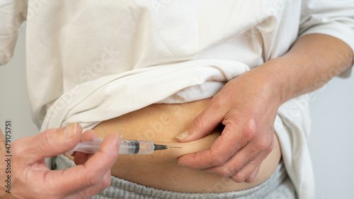 A woman in light clothes, giving herself an injection in the stomach, on a white background. He holds a syringe with medicine in his hand. Vaccination. An injection. Virus protection. Close-up.