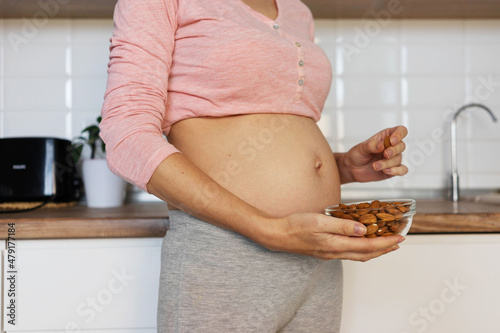 pregnant woman holding a bowl of nuts in her hand on the background of the home interior. Concept of healthy eating during pregnancy