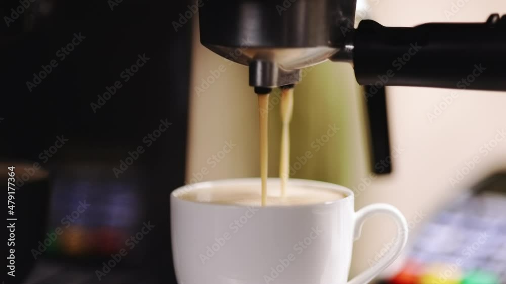 Espresso machine pouring coffee. Close up of espresso dripping into coffee mug. Espresso in a white cup. Tasty coffee. Caffeine. Coffeeshop in the background with credit card machine terminal NFC Espresso machine pouring coffee. Close up of espresso dripping into coffee mug. Espresso in a white cup. Tasty coffee. Caffeine. Coffeeshop in the background with credit card machine terminal NFC