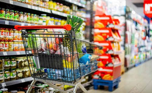Fotografering A shopping cart with grocery products in a supermarket