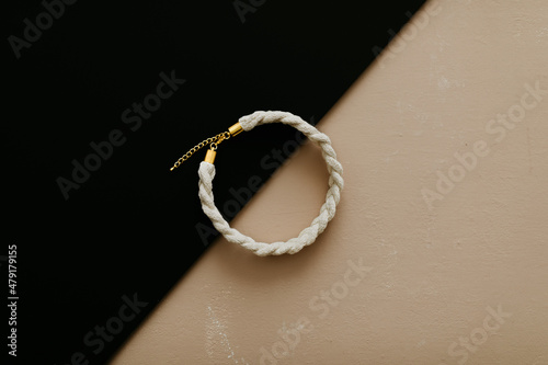 A white natural cotton necklace on beige and black background. Sustainable fashion accessory for girls and woman. Flat lay, top view. Copy space image. 