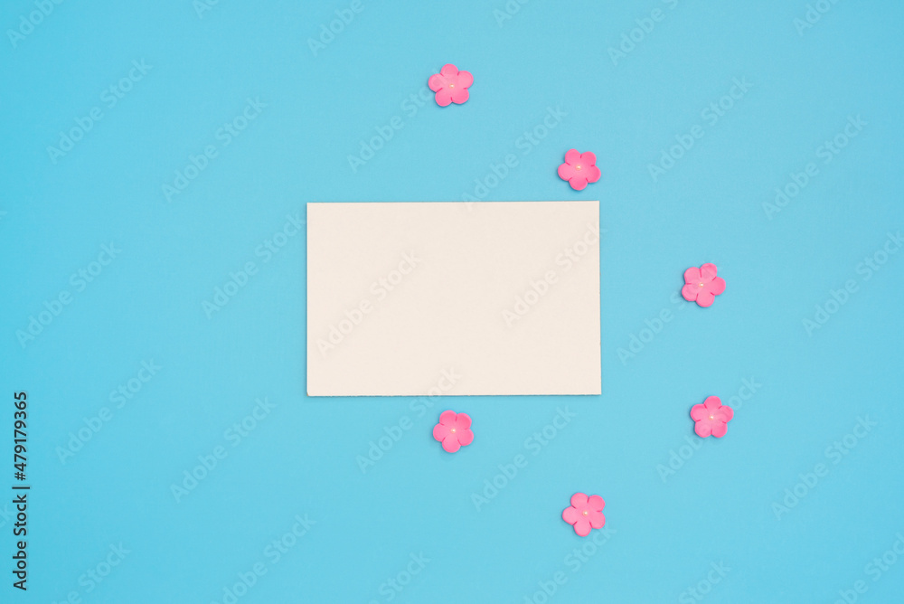 White paper card note with small pink flowers on blue background. Greeting card. Love, Valentines Day or other holiday concept. Flat lay style with copy space