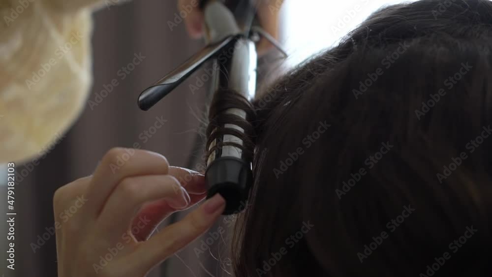 Hairdresser makes the girl's hair with a electric curling iron. Unrecognizable caucasian woman curls her hair, styling. Preparing for the holiday.