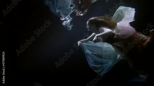 underwater fairytale, graceful lady in silk dress is swimming under water surface