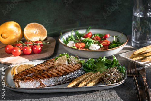 Grilled salmon steak, mini corn, microgreen, salad and lemon on wooden table. Fried salmon steak and fresh salad and vegetables