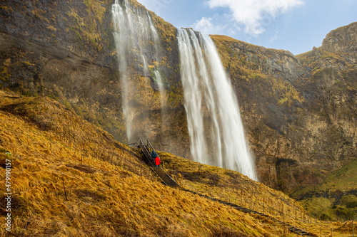 Panoramic view of Seljalandsfoss waterfall and tourists ascending to the observation deck.