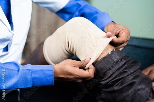 Close up shot of unrecognizable Physician treating old man by wearing stretch bandage for knee sprain or joint paint- concept of senior people muscle injury, healthcare treatment.