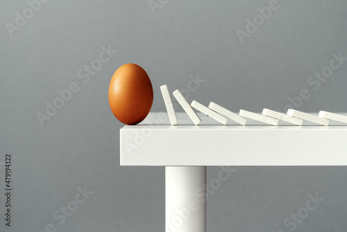 Obraz na plátně Egg on the edge of a table about to fall due to domino tiles pushing each other