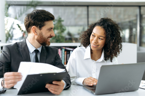 Two successful multi-ethnic colleagues are working together on a project. Caucasian successful man, ceo company discussing business strategy with African American female colleague in modern office