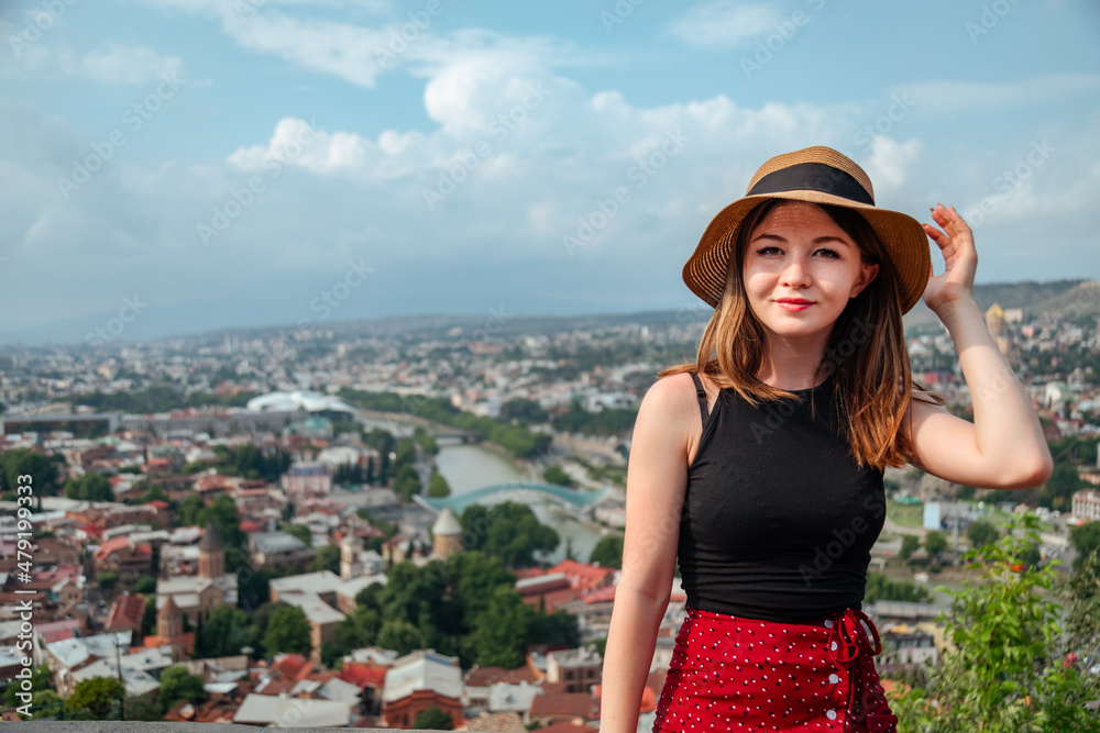 Beautiful woman in hat standing at Tbilisi city panorama at and looking at the camera