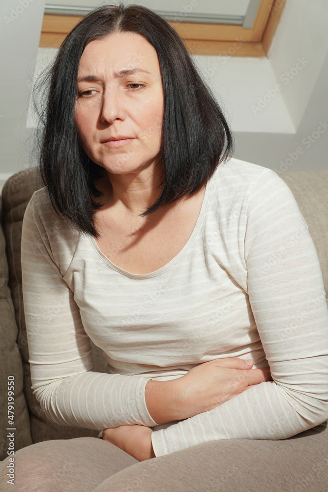 Middle aged mature woman suffering from stomach ache at home. Abdominal
