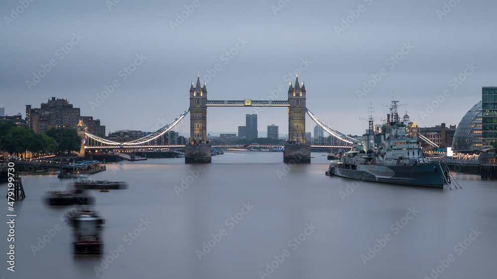 Tower Bridge, spanning the river Thames, London, England.  The day is cloudy and the water is smooth from a long exposure. 