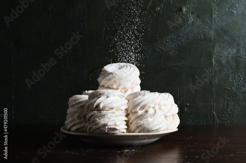 Lots of marshmallows on a plate sprinkled with powdered sugar, on a dark background with a place to insert text