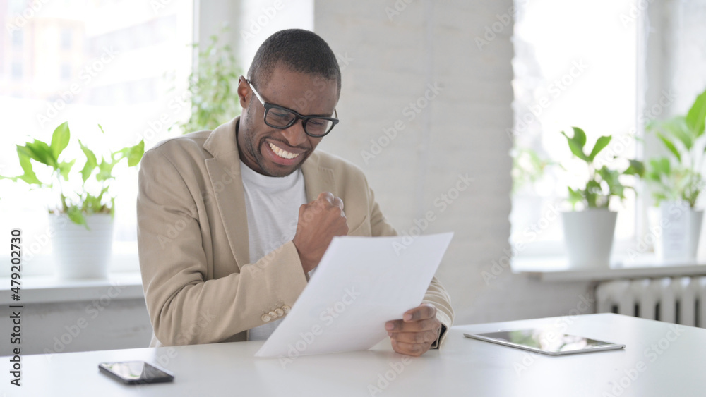African Man Celebrating Success while Reading Documents in Office African Man Celebrating Success while Reading Documents in Office