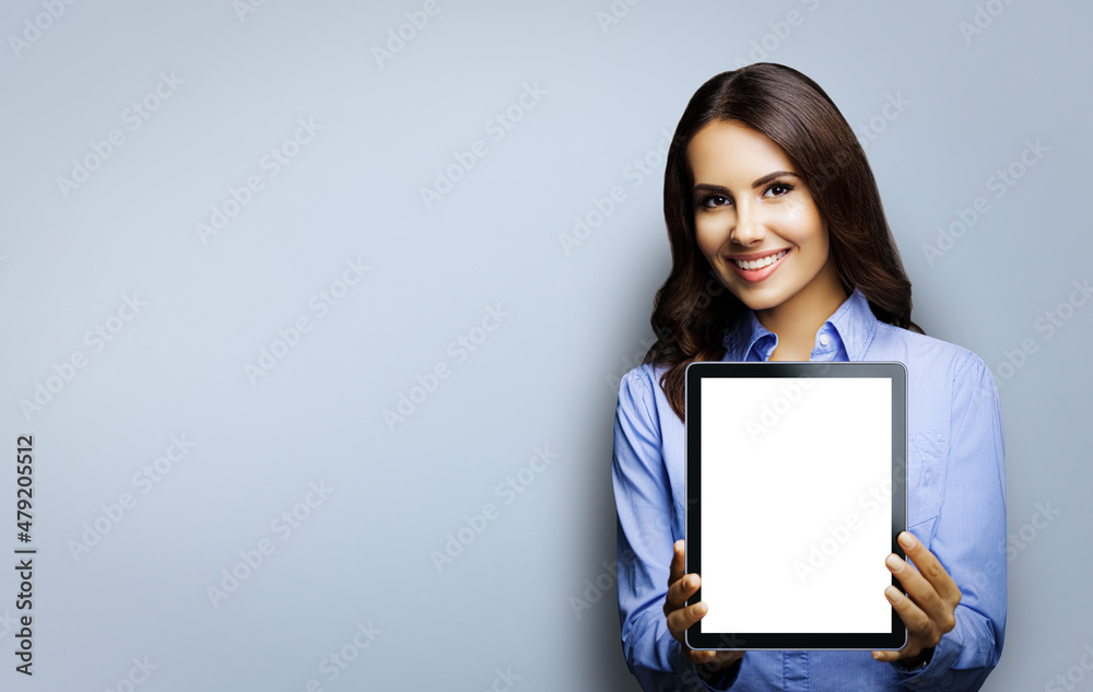 Portrait of happy smiling brunette businesswoman showing mock up blank tablet pc, touchpad, with copy space area, isolated over grey background. Confident young business woman at studio Portrait of happy smiling brunette businesswoman showing mock up blank tablet pc, touchpad, with copy space area, isolated over grey background. Confident young business woman at studio
