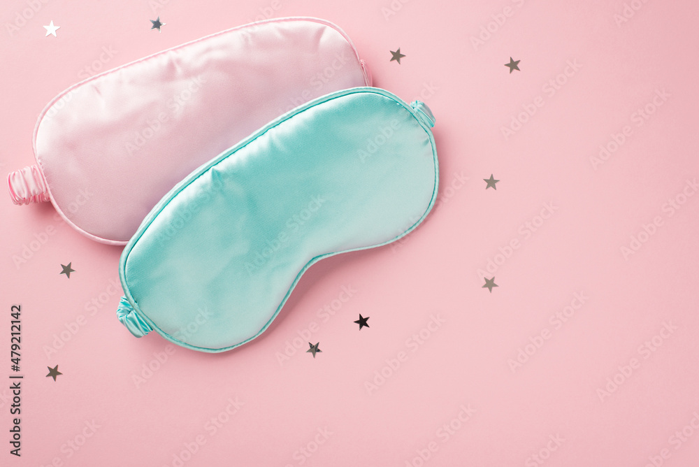 Fototapeta premium Top view photo of two light pink and blue silk sleeping masks and star shaped confetti on isolated pastel pink background with empty space