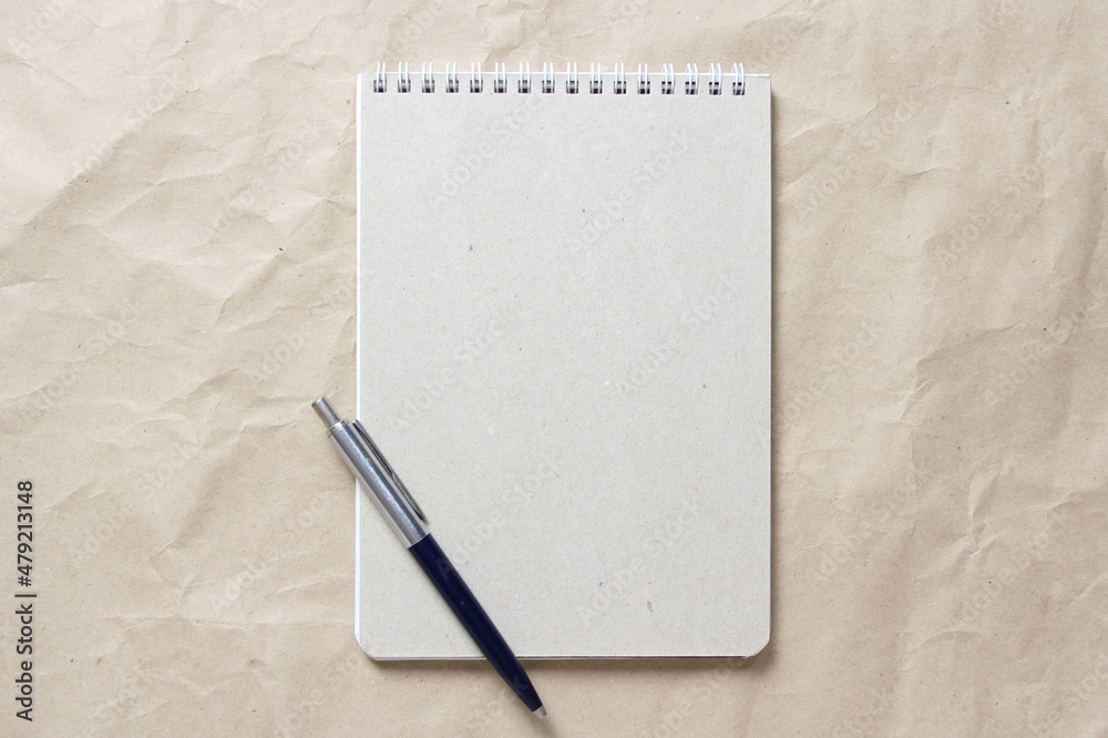 Gray notepad with white coiled spring and pen on a background of beige crumpled craft paper. With empty space for text and design Gray notepad with white coiled spring and pen on a background of beige crumpled craft paper. With empty space for text and design