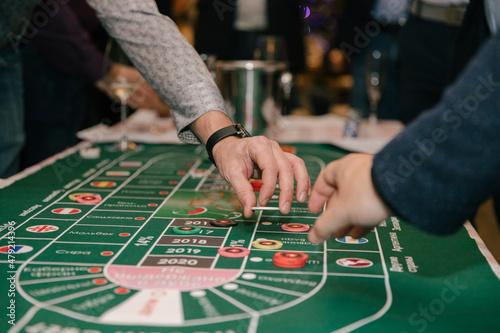 Close-up, hands of people playing in a wine casino, a man's hand with game chips on a green background of the table. Casino concept