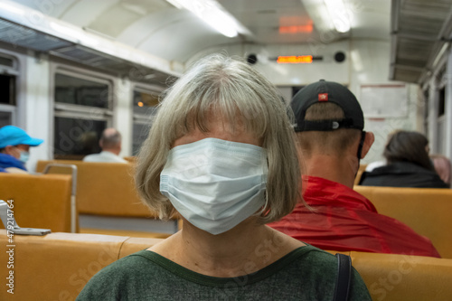 Medical mask on a woman's face. Threats of coronavirus infection in public transport. People on the train during the Covid-19 pandemic.