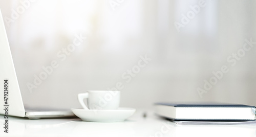 There is a laptop on the desktop, a cup of coffee and a diary. Side view.