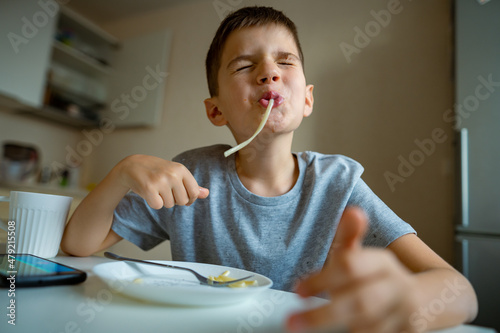 Boy, child eating macaroni, retraction long pasta into his mouth photo