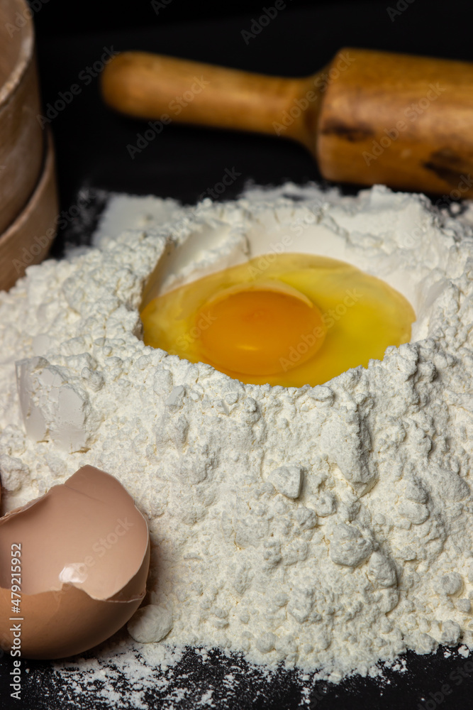 Raw egg in flour on a black background. Dough preparation. homemade baking