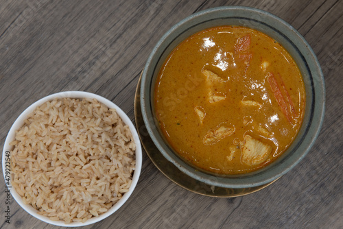 Overhead view of spicy hot bowl of yellow curry with chicken served with a side order of brown rice for a delicious Thai food meal