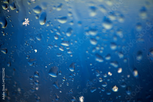 Abstract background with rain drops and snowflakes on car window, wet glass, rainy day.