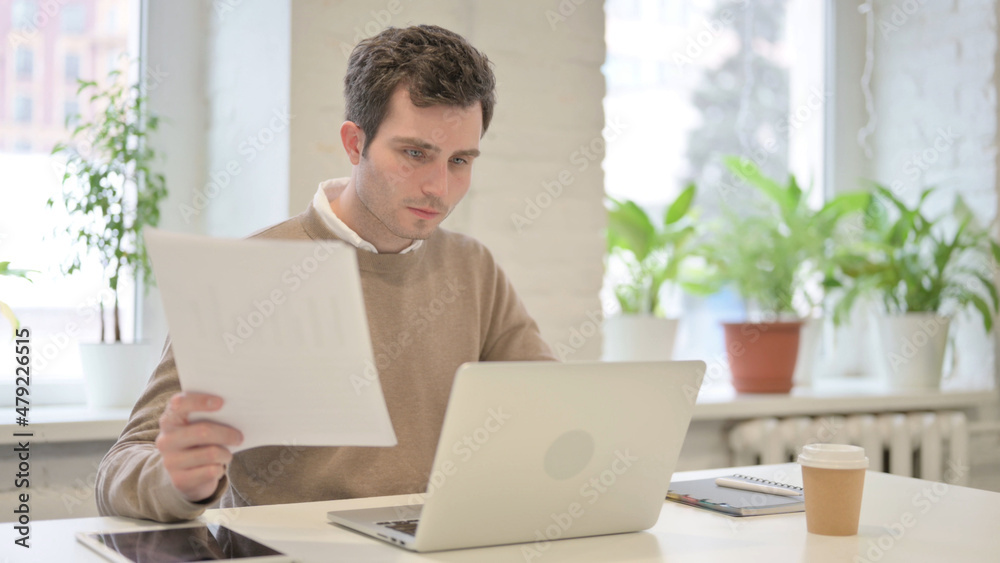 Man with Laptop Reading Documents in Office Man with Laptop Reading Documents in Office