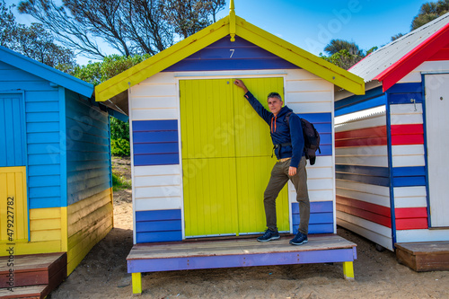 Happy tourist touching a colorful hut in Brighton Beach, Australia.