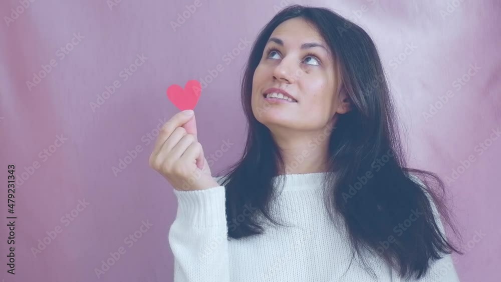 Smiling funny young brunette in a white sweater smiles, blinks and waving red hearts on a pink background. Valentine's Day Smiling funny young brunette in a white sweater smiles, blinks and waving red hearts on a pink background. Valentine's Day