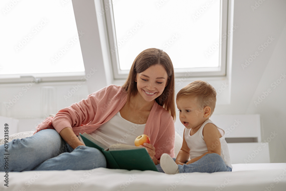 Smiling mother reading a book the baby in bed