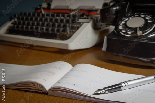 Checkbook, ink pen, retro typewriter and old telephone on the table.  Selected focus