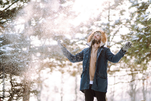 Handsome bearded young man standing outdoors fur hood in winter season forest. Season holiday leisure. Nature.