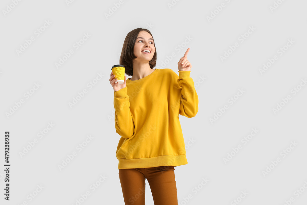 Beautiful woman with cup of coffee pointing at something on light background Beautiful woman with cup of coffee pointing at something on light background