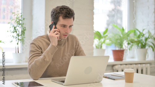 Man Talking on Smartphone while using Laptop in Office