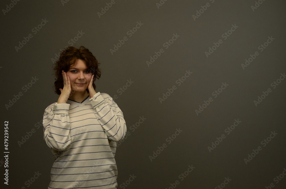 Portrait of surprised cute young girl standing isolated on gray background. Looking at the camera. Hands next to open mouth. Astonishment. Space for text Portrait of surprised cute young girl standing isolated on gray background. Looking at the camera. Hands next to open mouth. Astonishment. Space for text