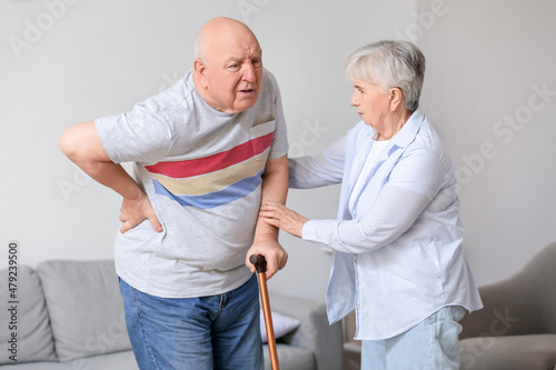 Senior man with walking stick suffering from back pain and his wife at home