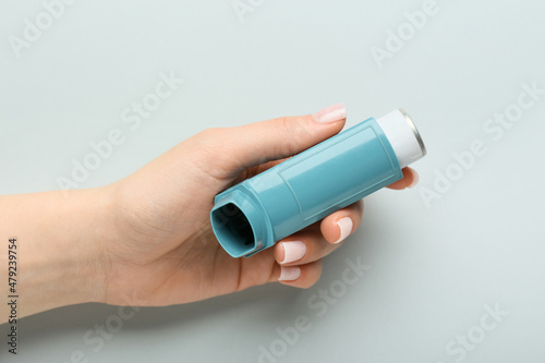 Female hand with modern asthma inhaler on grey background