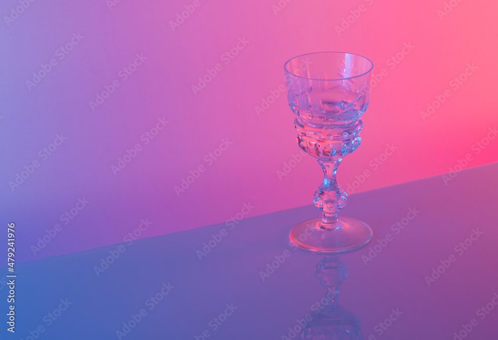 Glass against neon iridescent pink and blue colors. Minimal party life concept. Glass against neon iridescent pink and blue colors. Minimal party life concept.