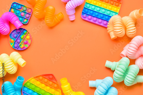 Frame made of colorful Pop Tubes and Pop it fidget toys on orange background