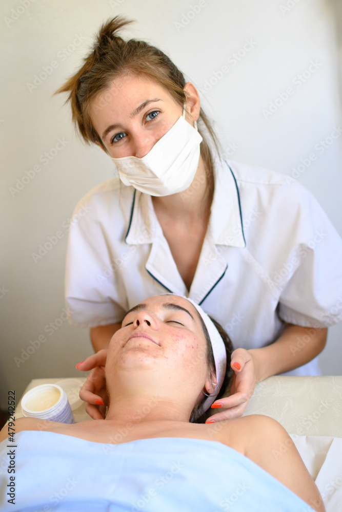 Young caucasian woman doctor looking at the camera and smiling while massaging the face of another young caucasian woman. Young caucasian woman doctor looking at the camera and smiling while massaging the face of another young caucasian woman.