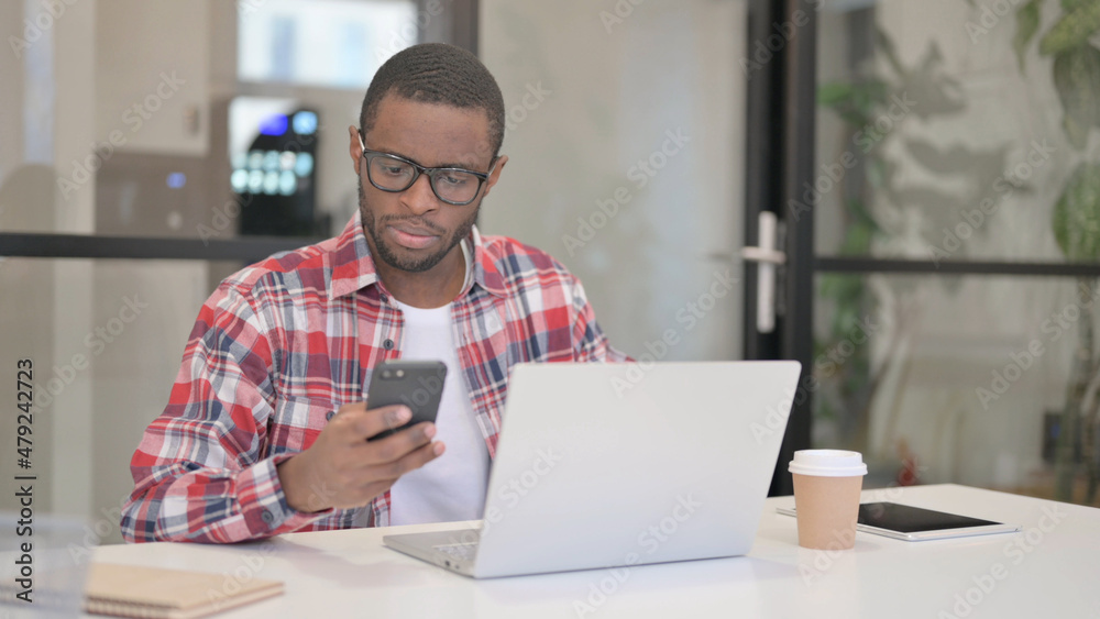 African Man using Smartphone while using Laptop African Man using Smartphone while using Laptop