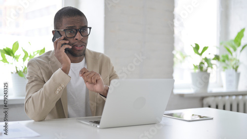 African Man Talking on Smartphone while using Laptop in Office